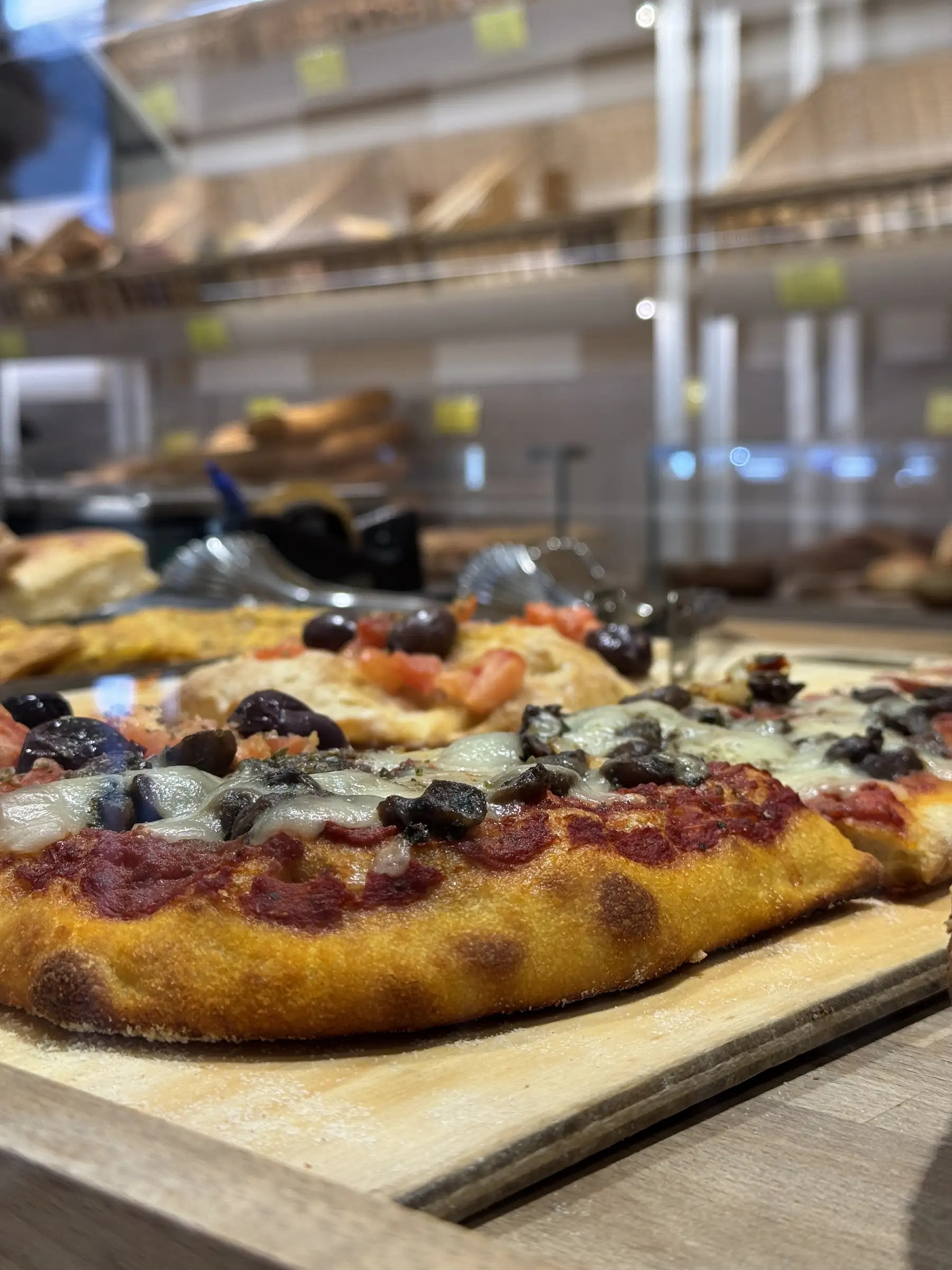 Pizza in teglia con pomodoro, mozzarella e olive, appena tagliata sul tagliere del banco